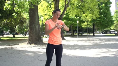 Young woman sets smartwatch and starts jogging in city park super slow motion