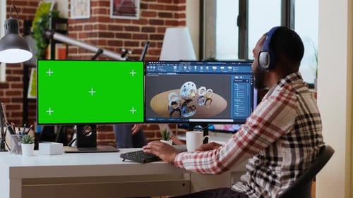 Software Developer Creates a Gear Prototype on Dual Monitors Next to Chroma Key