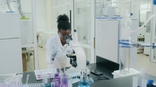 Young Adult Scientist Works with Microscope in Laboratory