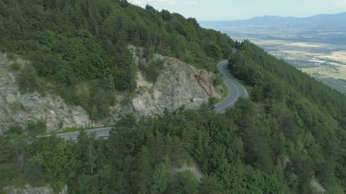 Black SUV driving at mountain highway with beautiful forest around the road. Aerial drone view of mo