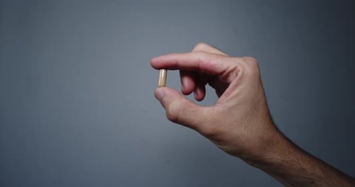 Hand Holding Medicine Capsule Against Gray Background