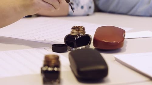 Female hand writting oldschool black ink pen on the white sheet of paper close up slow motion