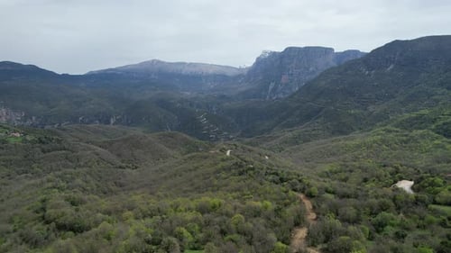 Aerial view of a serene mountain village with lush greenery and snow-capped peaks in the background.