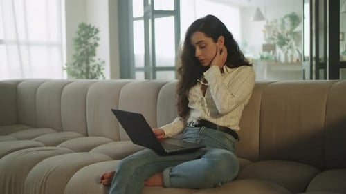 Woman Uses Laptop on Couch, Appears Tired