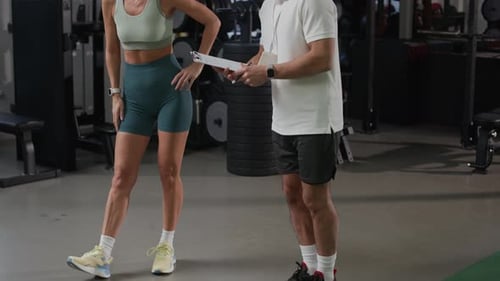 Coach Demonstrating Exercise to Adult Woman during Individual Training in Gym