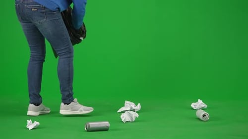 A Female Volunteer Wearing Black Gloves and Carrying a Trash Bag Picks Up Trash on the Green Screen