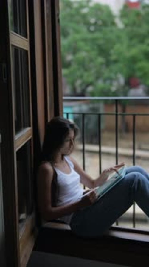 A Woman in Casual Wear is Peacefully Reading By the Window Enjoying a Quiet Moment