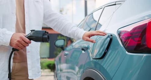 Nahaufnahme männlicher Hände, die auf dem Parkplatz im Freien das Ladegerät an ein Elektroauto anschließen