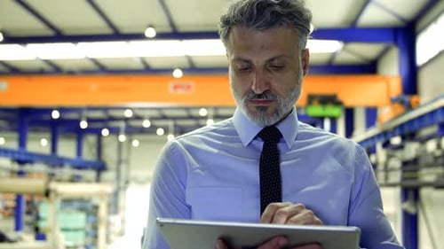 Ein Industriemann-Ingenieur, der in einer Fabrik steht und ein Tablet benutzt.