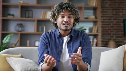 Webcam view. Young man talking on a video call looking at camera sitting on sofa in living room