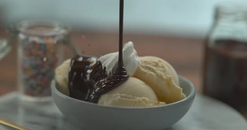 Schokoladensauce wird auf eine Schüssel mit Eiscreme und Schlagsahne gegossen