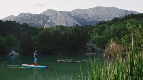 Man Sailing on SUP on Small Lake in Mountains