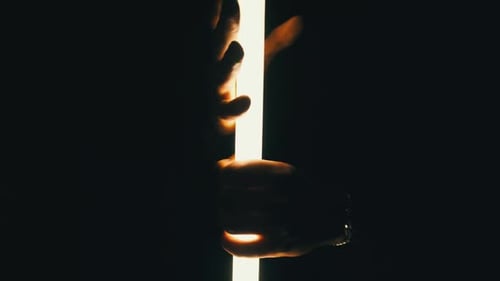 Male Hands Hold a Neon Lightsaber Against a Black Background