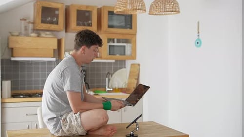 Home Office Setup A Young Man Skillfully Working on His Laptop in a Stylish Modern Kitchen Space
