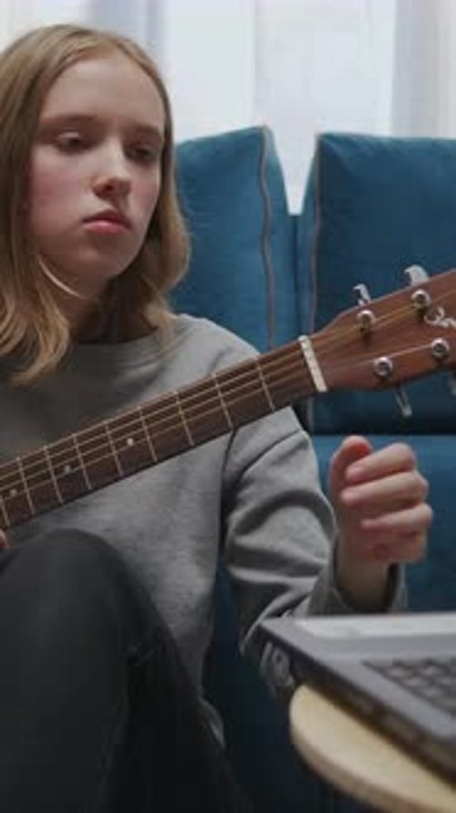 Teen Girl Practicing Acoustic Guitar at Home While Watching Online Lesson on Laptop Learning Chords