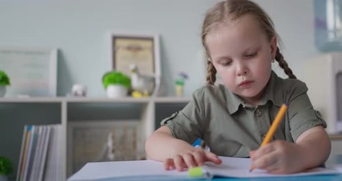 Jeune écolière aux cheveux tressés se concentrant sur l'écriture dans un cahier à un bureau de classe