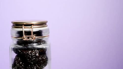 An airtight mason jar rotating with dried plums on a neon lilac background. Flat plane. Eye level