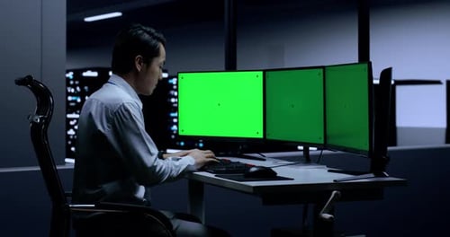 Asiatischer männlicher Programmierer setzt sich hin und tippt auf Greenscreen-Desktops im Serverraum