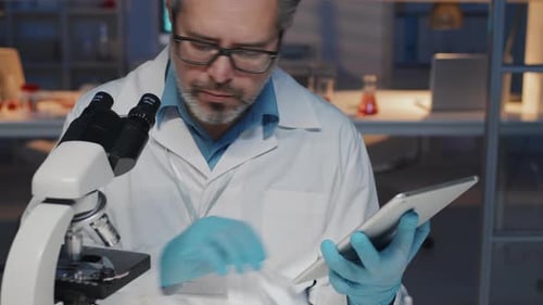 Serious Experienced Scientist with Tablet Studying New Substance in Microscope
