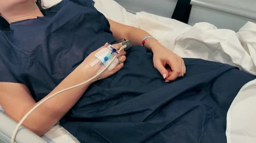 Patient Lies in Bed in the Hospital with Intravenous Drip in the Hand After Surgery Healthcare and