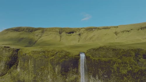 Rising shot of a tall waterfall in Iceland. The river stream is slowly flowing to the mountain edge.
