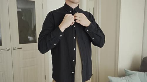 Man Buttons Up Stylish Dark Shirt in Bedroom