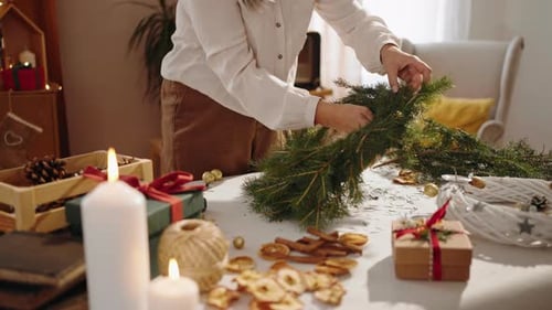 Woman Arranging Christmas Wreath Decorations on Table Indoors