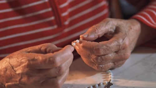 4K video of an elderly women holding the holy rosary and praying next to the Holy Bible. Indoor scen