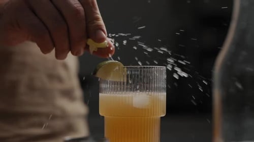 Junges Männchen, das Limette oder Zitrone über einen frisch gemischten Cocktail in einem Trinkglas auspresst 4K Zeitlupe Schließen
