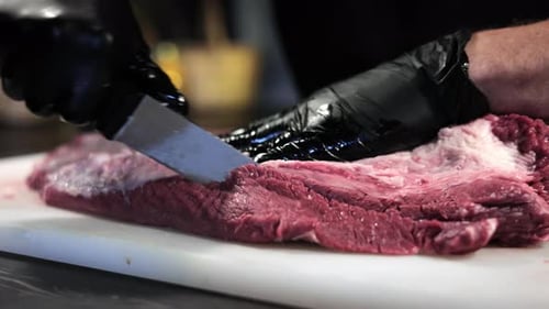 Gloved Person Precisely Slicing Raw Steak With Knife