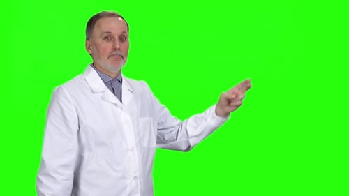 Mature Doctor in Lab Coat Pointing on Green Screen