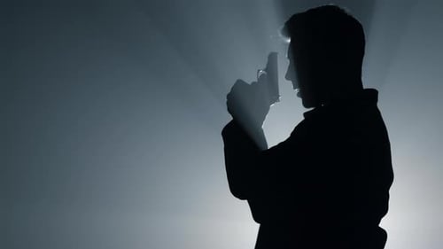 Silhouette of Dangerous Man Shooting with Gun in Floodlight Background. Side View