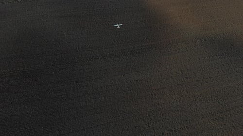 White radio control plane flying over brown fields. Drone shot in UHD.