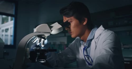 Young Adult Scientist Looking Through a Microscope in Lab