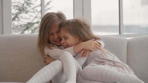 Two Little Girls Laughing and Hugging on Couch