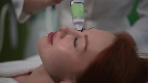 Primer plano de una esteticista que utiliza un dispositivo de microagujas realizando un procedimiento de rejuvenecimiento a una paciente femenina