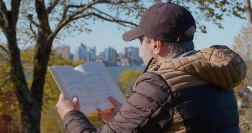 Mann liest ein Buch und sitzt bei Sonnenuntergang im Park im Gras