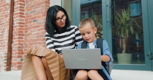 Woman and Child Using Laptop Outside School