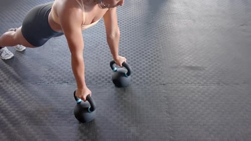 Performing push-ups with kettlebell, woman exercising in gym for fitness training, copy space