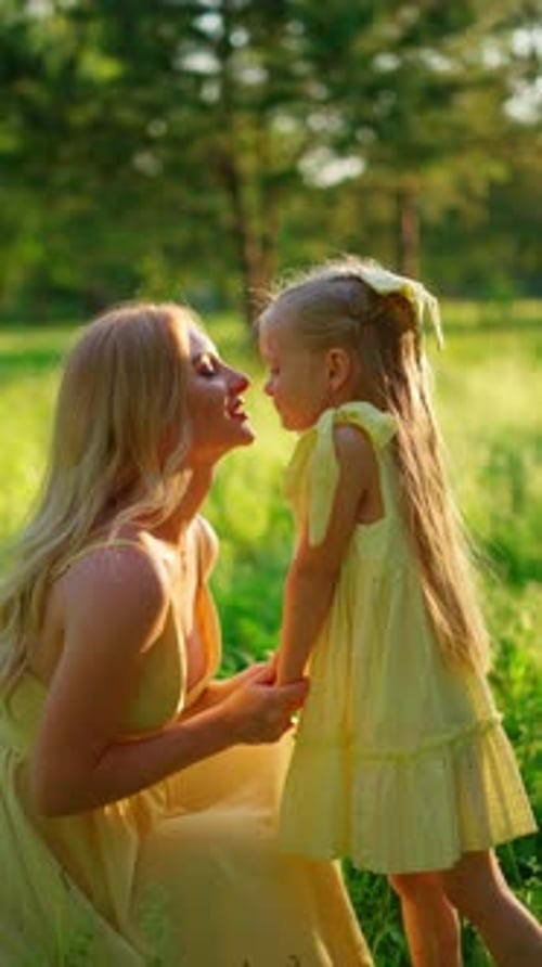Mother and Daughter in Identical Yellow Dresses on a Green Meadow Concept of Happy Family Moments