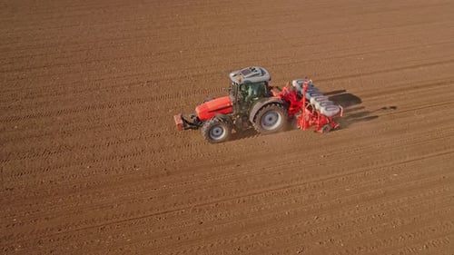 Aerial drone shot of a farmer in tractor seeding, sowing agricultural crops at field.