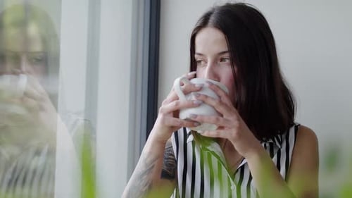 Thoughtful Woman Drinking Coffee by Window Indoors