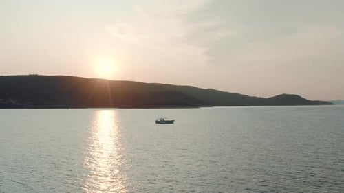 Aerial video of a small fishing boat docked in the middle of the sea in the evening.