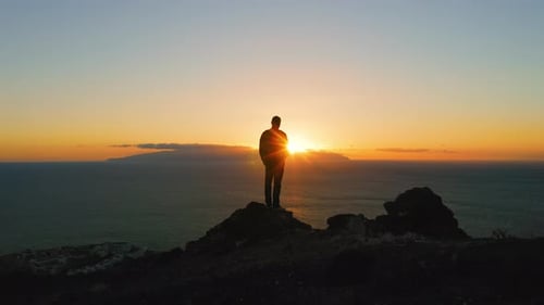 Man Standing on Top of Rock with Epic Mountain Viewpoint Colorful Sunset Light and Endless Ocean
