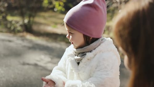 Child in White Coat Talks to Adult Outdoors