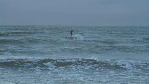 Man engaged in kitesurfing, overcast winter day, high waves, Baltic Sea Karosta beach (Liepaja), slo