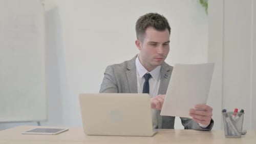 Smiling Man Working with Laptop and Paper at Desk