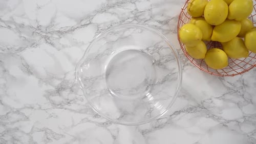 Zesting Lemon over Clear Bowl on Marble Surface