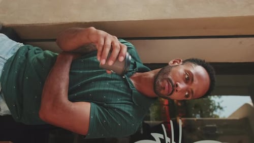 Young man drinking coffee while sitting in street cafe on cityscape background
