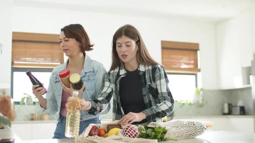 Dos amigas después de ir de compras, desempacar la comida para guardarla en la cocina, arreglar una bolsa de malla